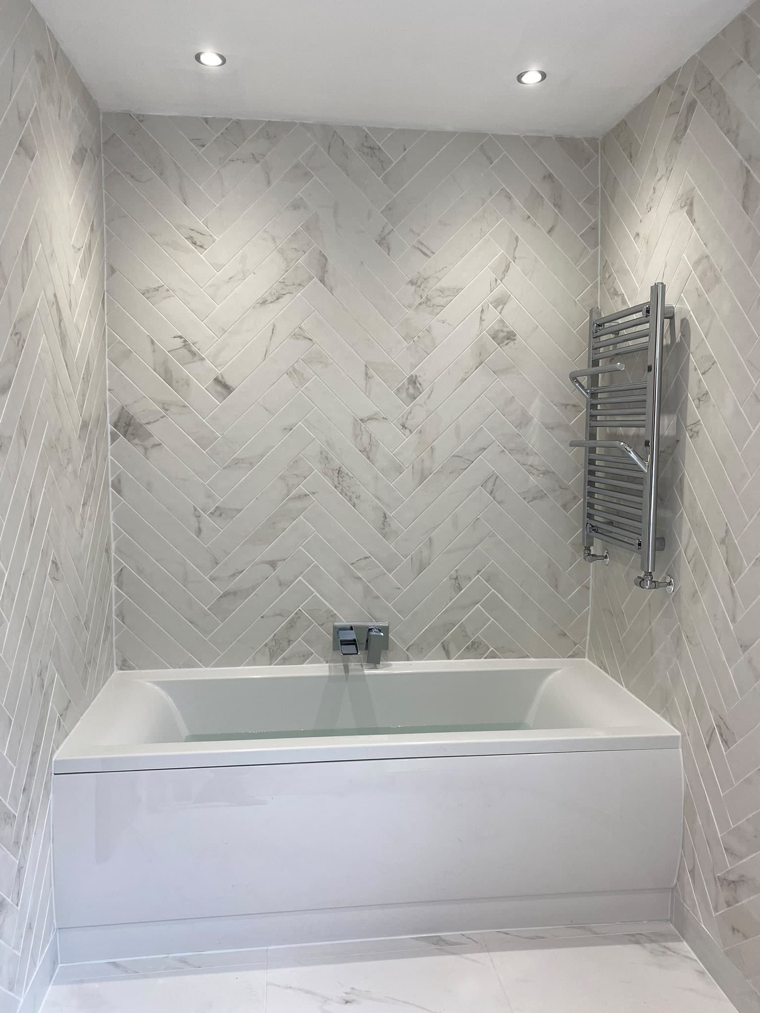 Bath with herringbone marble-effect tiles and a chrome towel rail