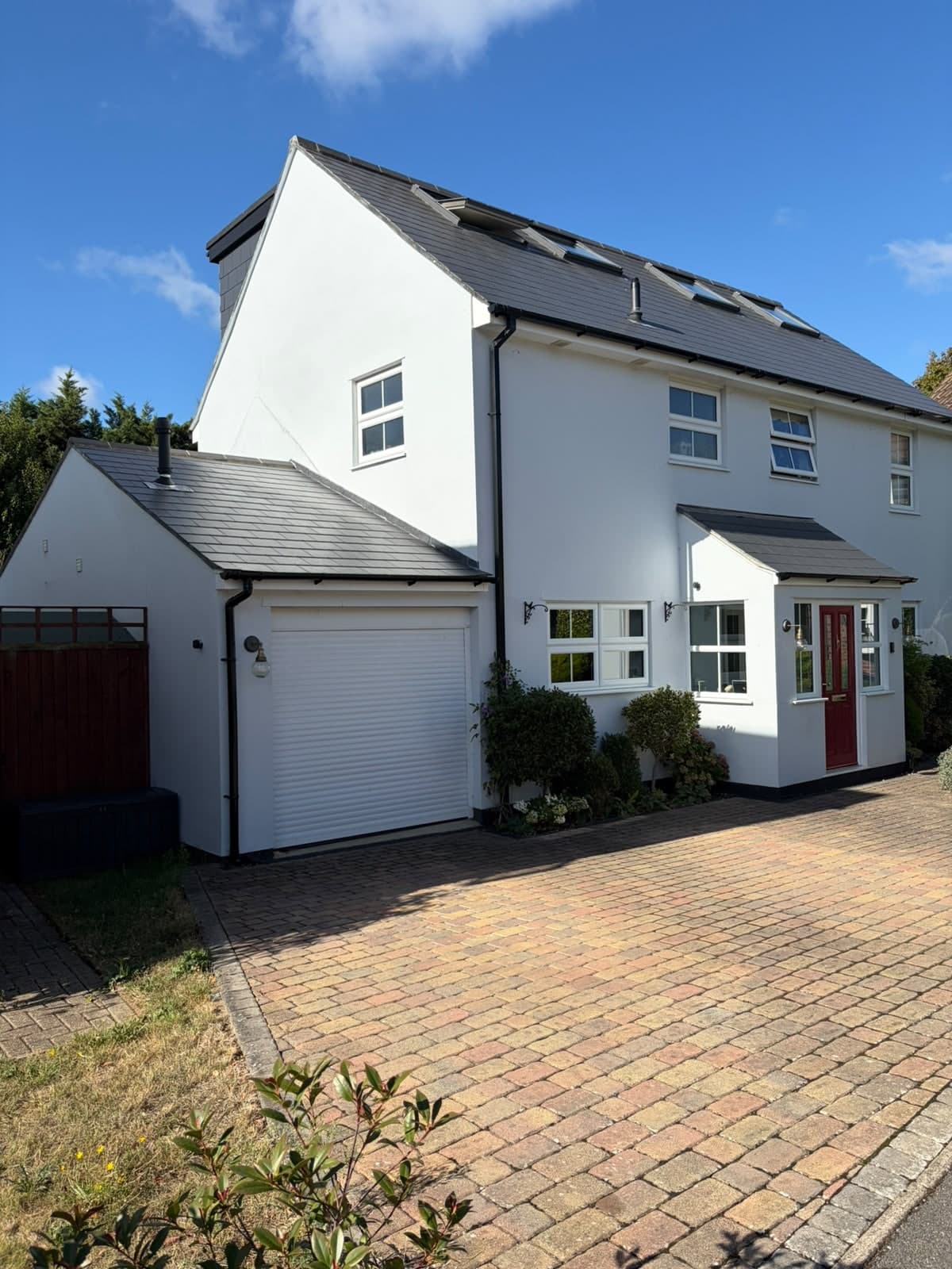 Front of the white rendered detached house with new garage door, porch and block-paved drive