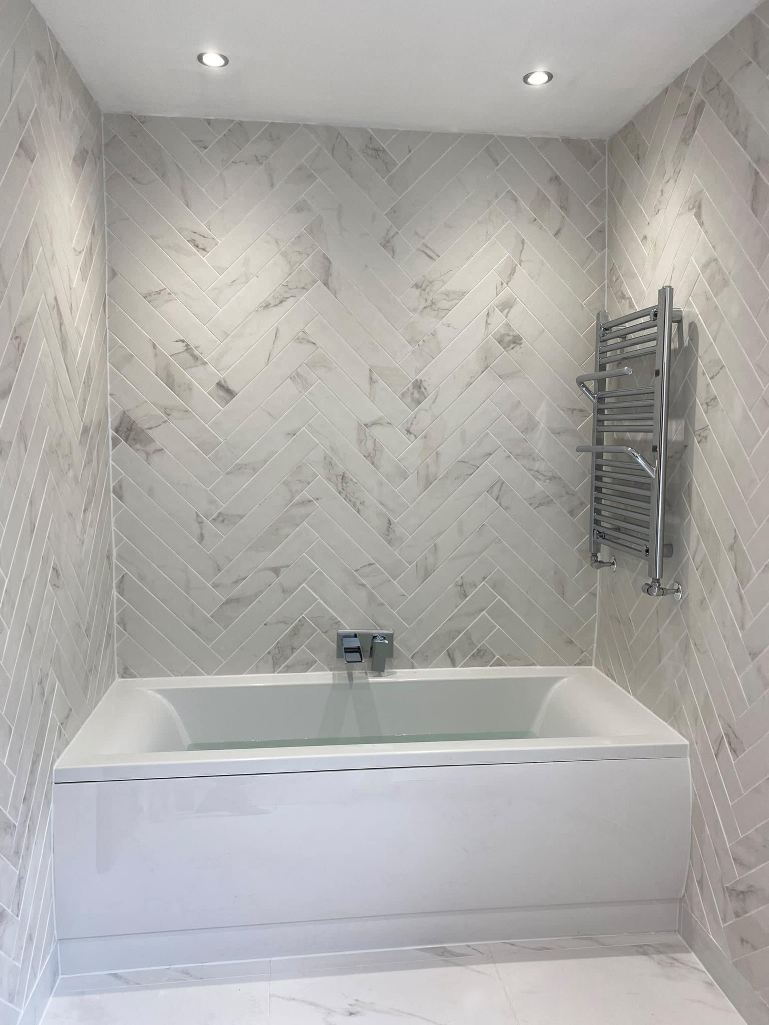 Bath with herringbone marble-effect tiles and a chrome towel rail